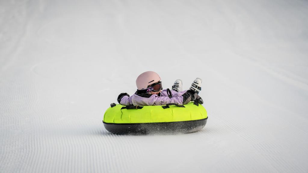 Ein Mädchen rutscht fröhlich mit dem Snowtube den verschneiten Hang hinunter und genießt die Fahrt.